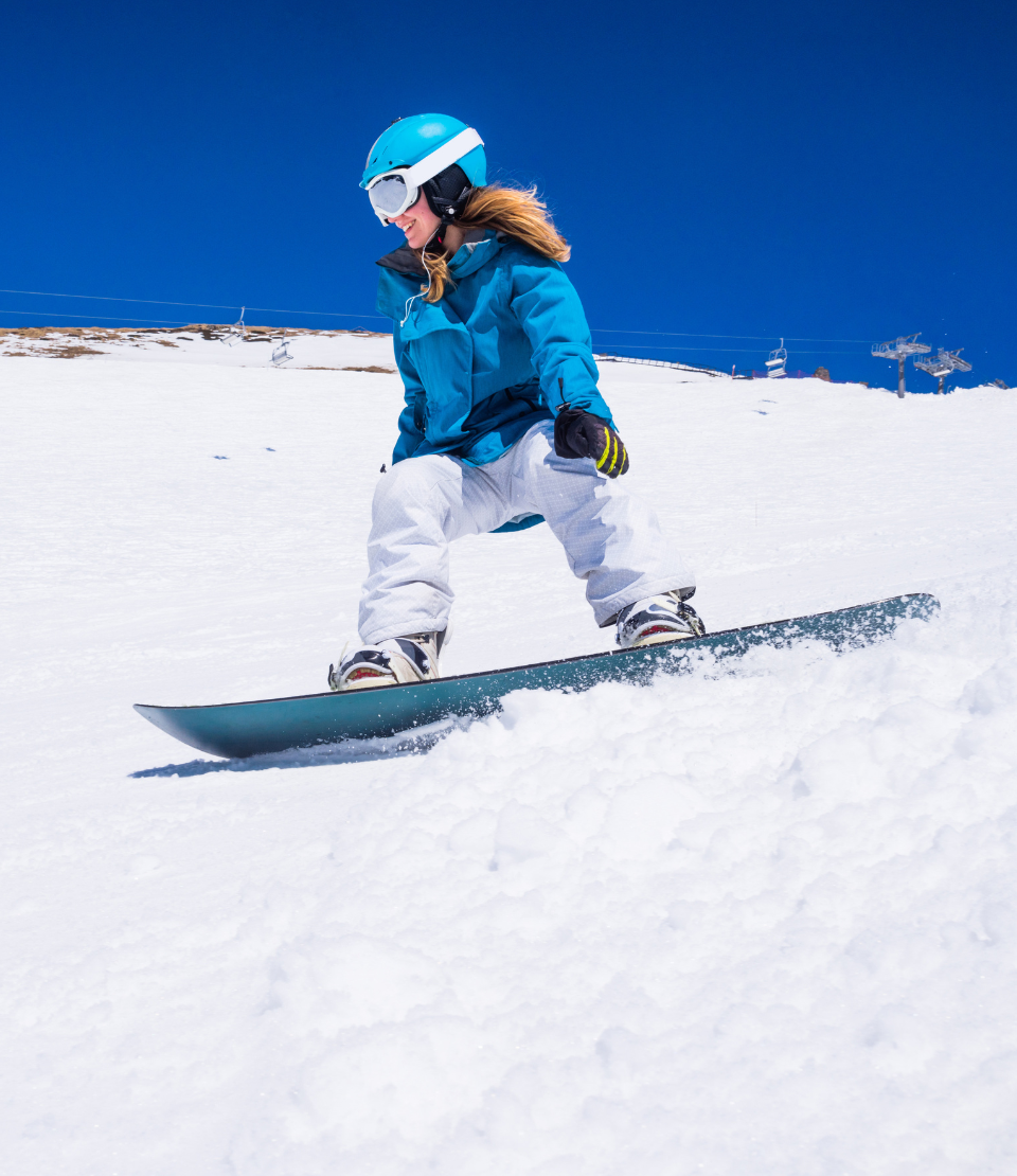 Woman snowboarding down a hill with snowboarding and skiing travel insurance