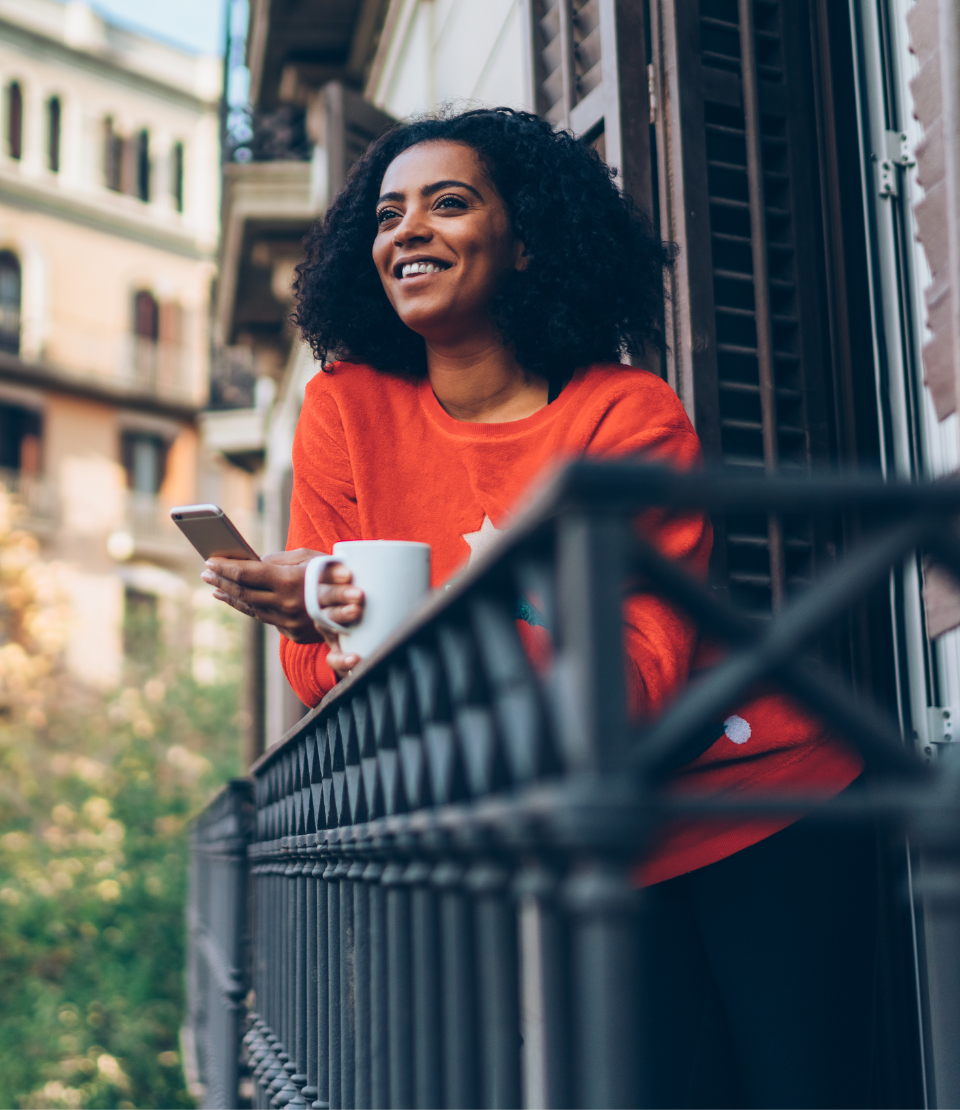 Woman standing on a balcony with coffee in Barcelona using her phone to learn more about Travelex