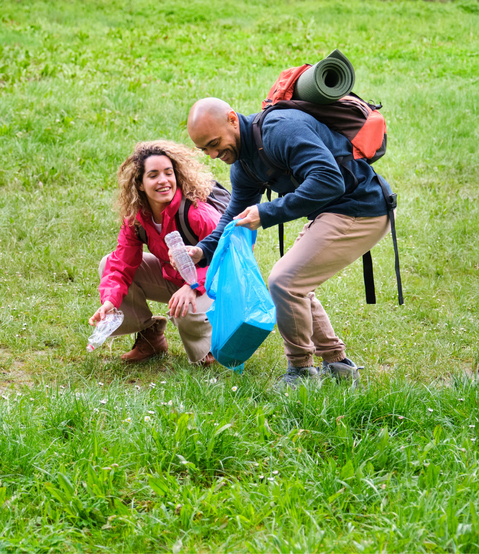 Man and woman smiling with camping backpacks on while picking up trash with volunteer travel insurance