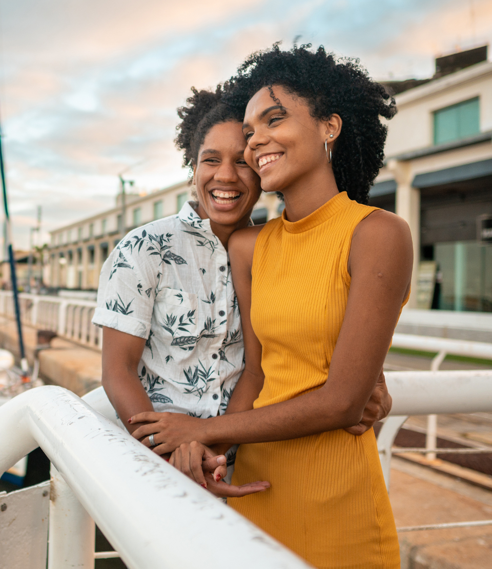 Two young women holding each other and looking at the ocean with a boat in the background in Marco Zero in Brazil