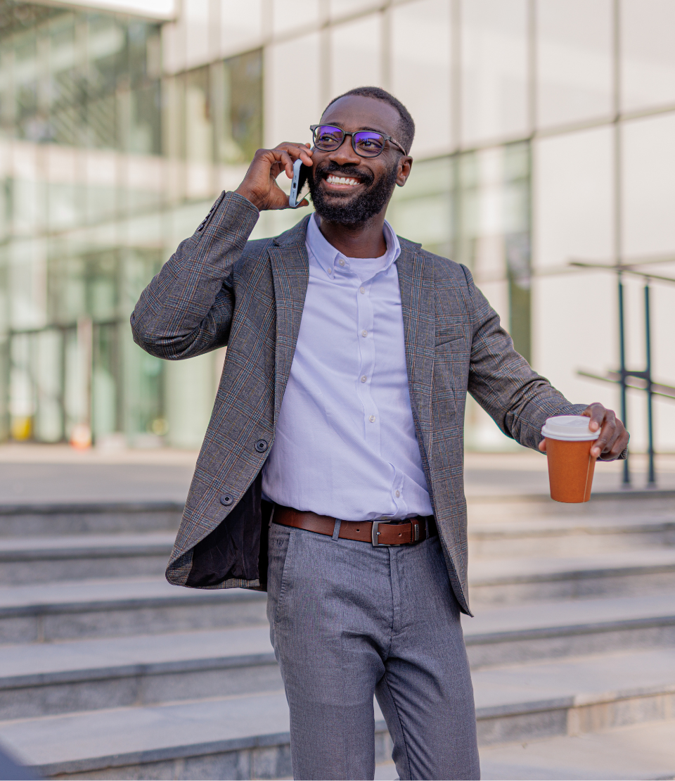 Man on the phone holding coffee and smiling in front of an office building with business travel insurance