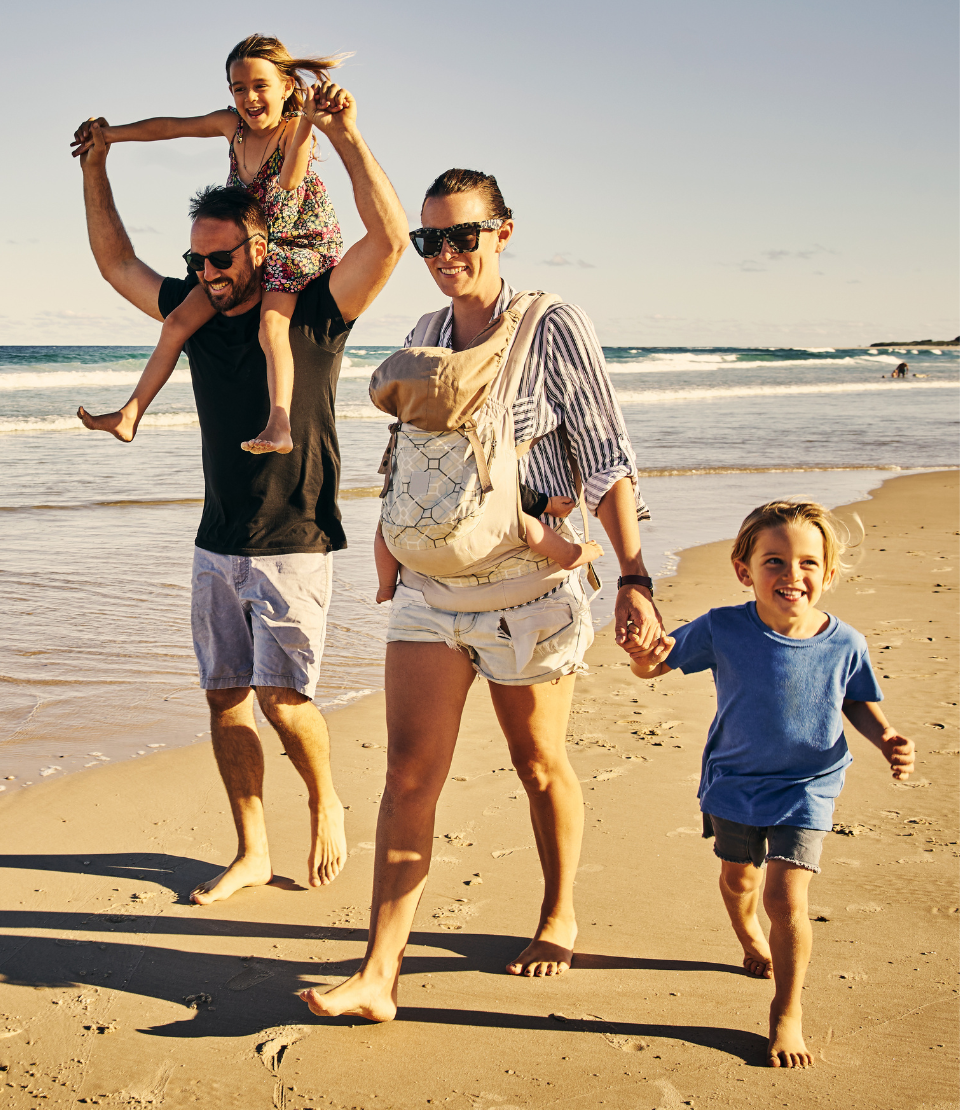 Man and woman with three young children walking together on the beach with family travel insurance