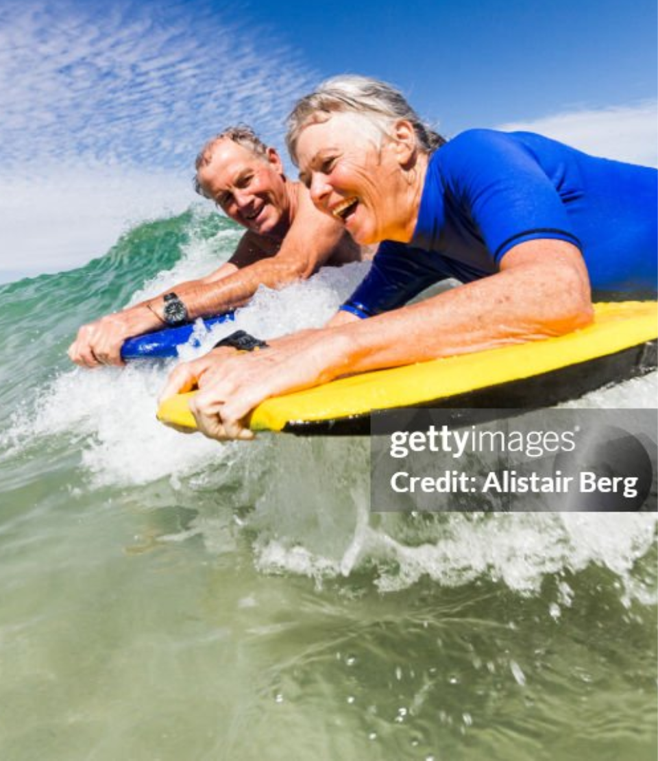 Senior man and woman boogie boarding on a wave in the ocean with senior travel insurance in Cape Town, South Africa