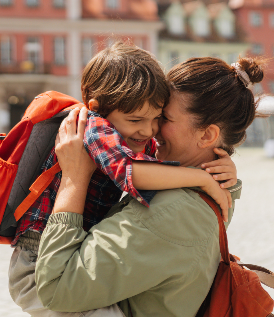 Woman smiling and hugging her young son wearing a backpack in Germany after reading Travelex insurance reviews