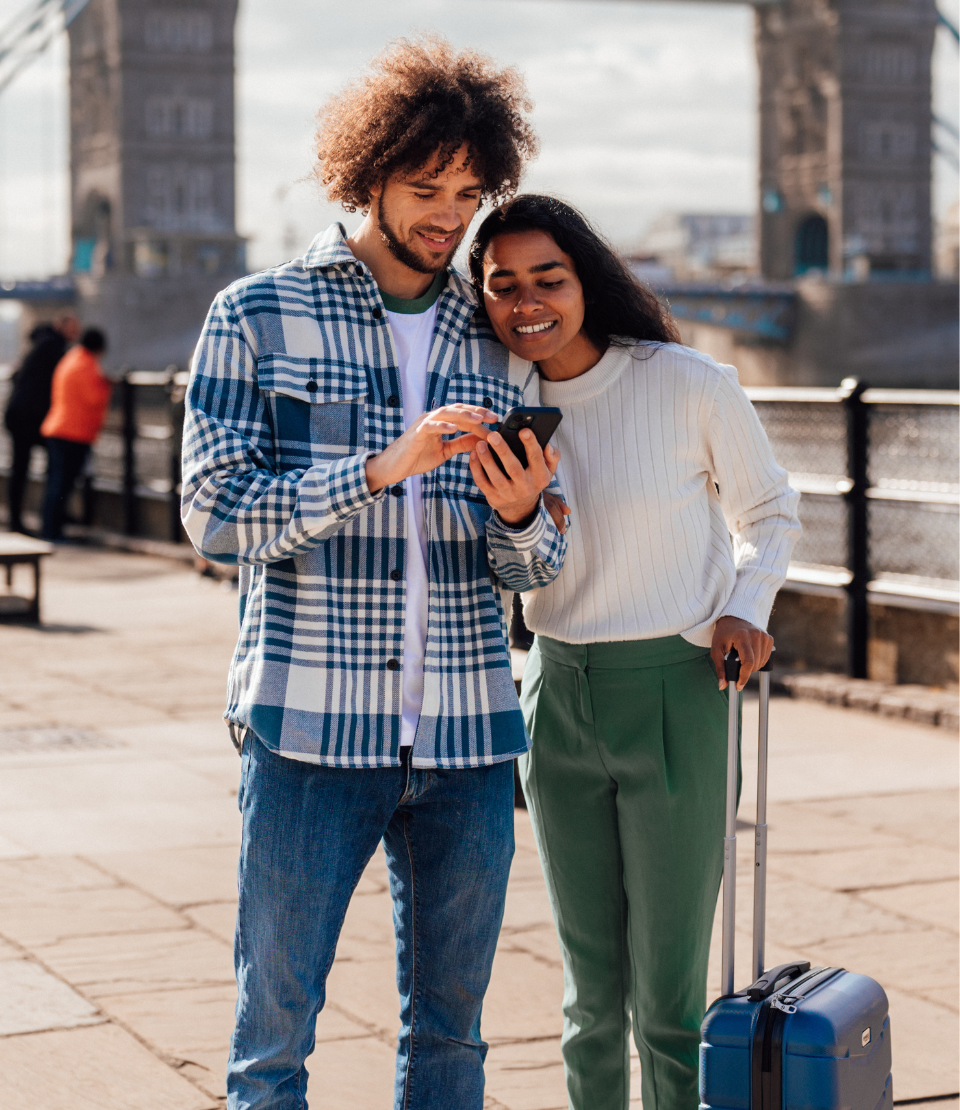 Couple in the U.K. in front of Tower Bridge smiling and looking at the Travelex Travel On app on their phone