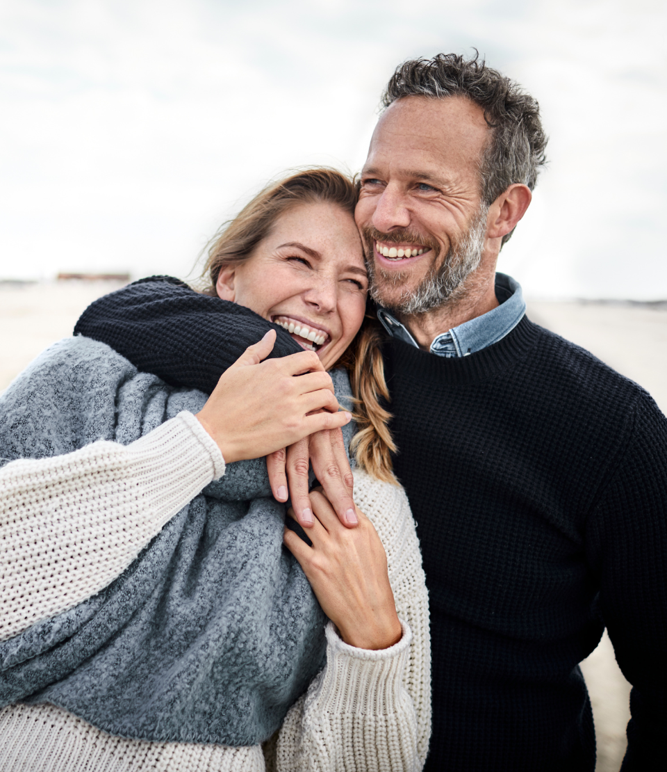 Middle-aged man with his arm around a middle-aged woman smiling on the beach