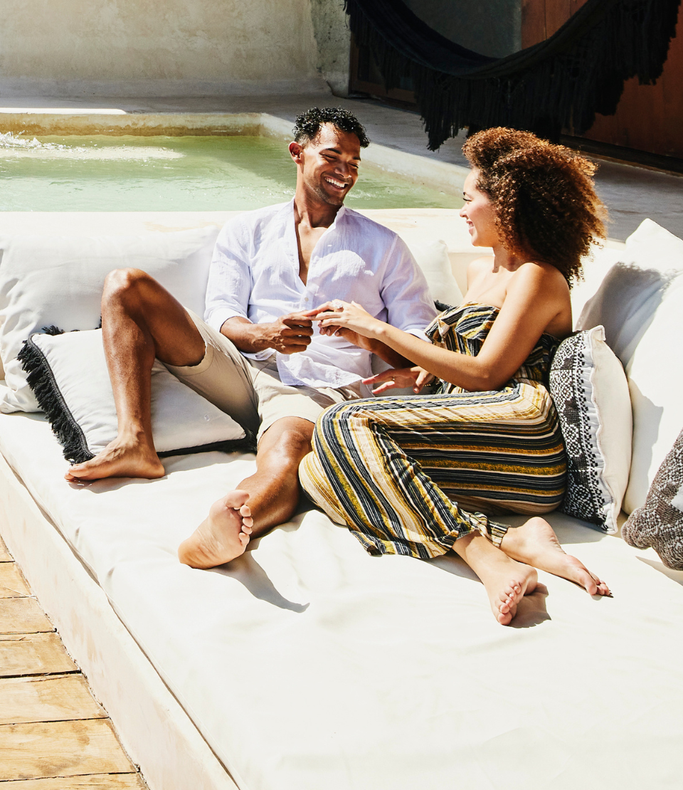 Smiling couple on an outdoor sofa at their accommodation overlooking the ocean in Quintana Roo, Mexico