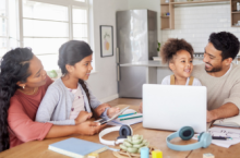 Family of four sitting at the kitchen table with a laptop looking at a travel insurance checklist.