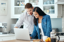 Smiling couple trying to calculate trip cost for their travel insurance policy.