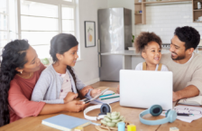 Family of four sitting at the kitchen table with a laptop looking at a travel insurance checklist.