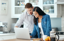 Smiling couple trying to calculate trip cost for their travel insurance policy.