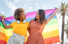 Two smiling women holding a pride flag during their LGTBQ+ travel.